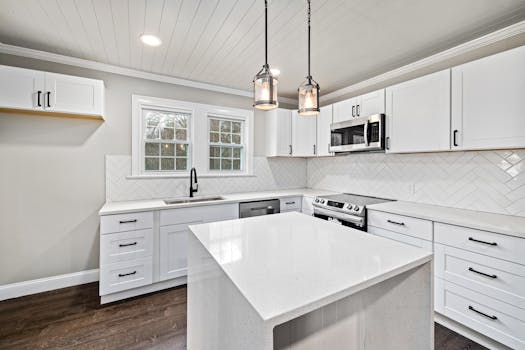Bright modern kitchen interior with white cabinetry, island, and pendant lights.