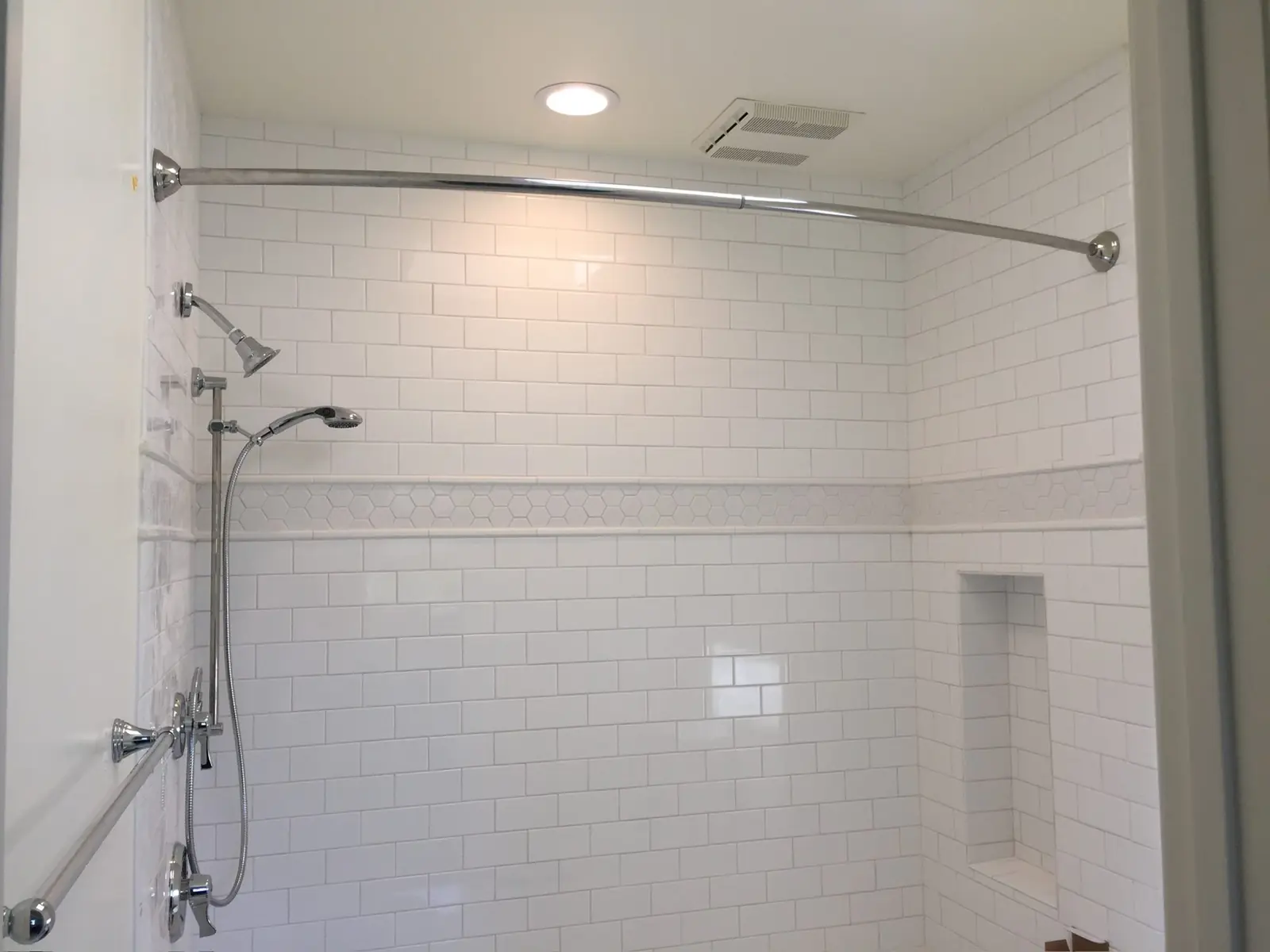 White subway tile shower with hex accent band and niche