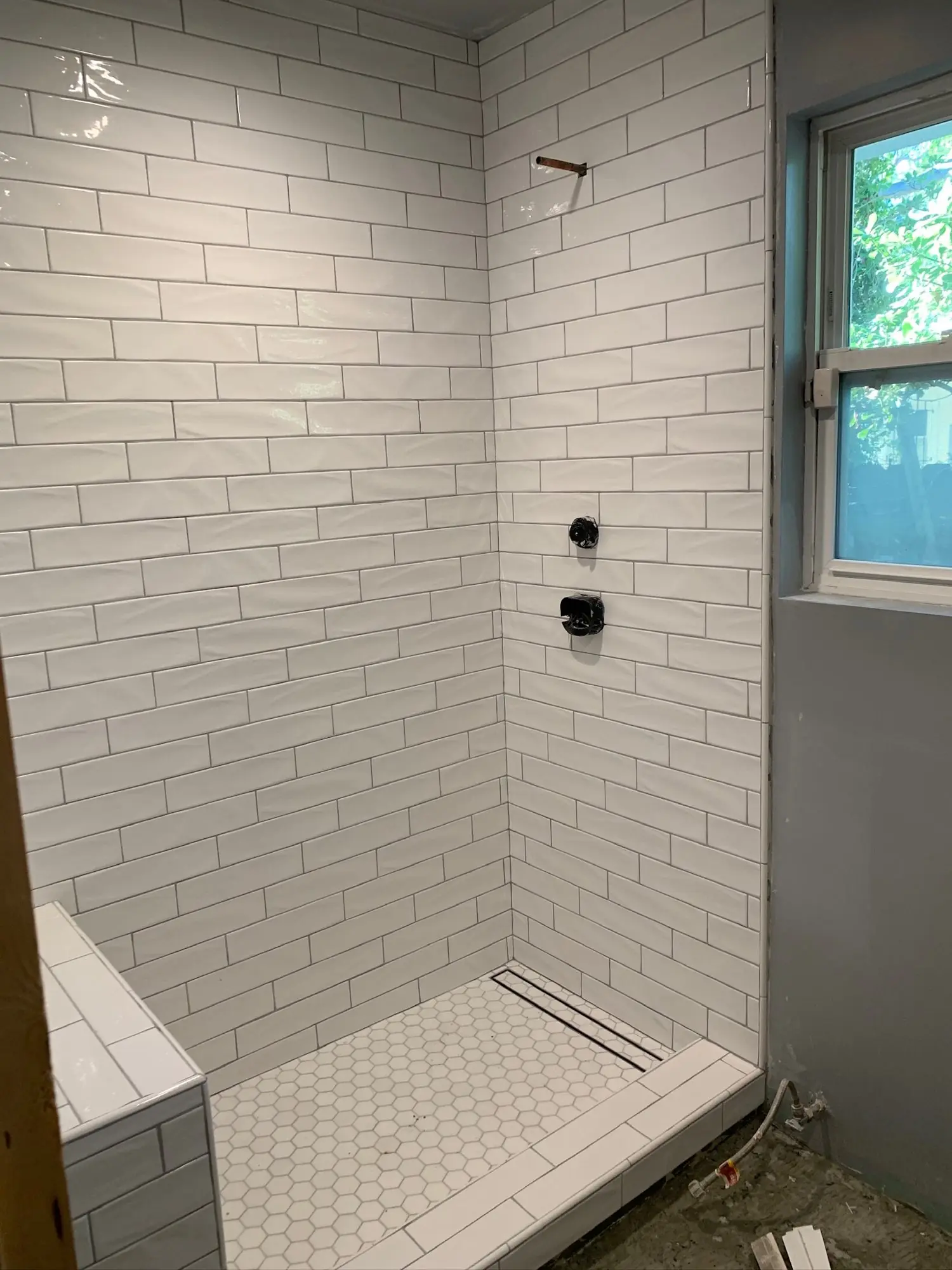 Subway tile shower with hex floor and linear drain during install