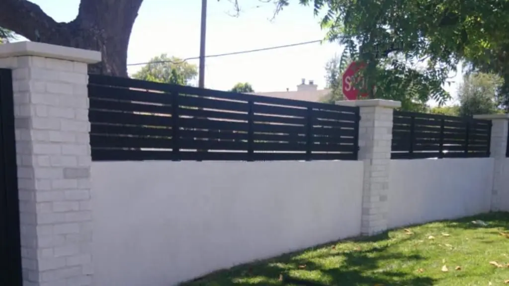 Slat fence panels between painted brick pillars on a stucco wall