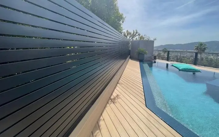 Aluminum slat privacy fence along a pool deck with composite decking