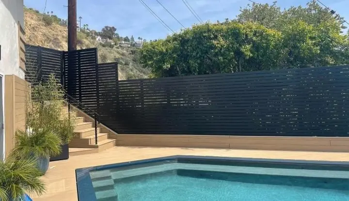 Stepped slat fence beside a pool and composite deck stairs