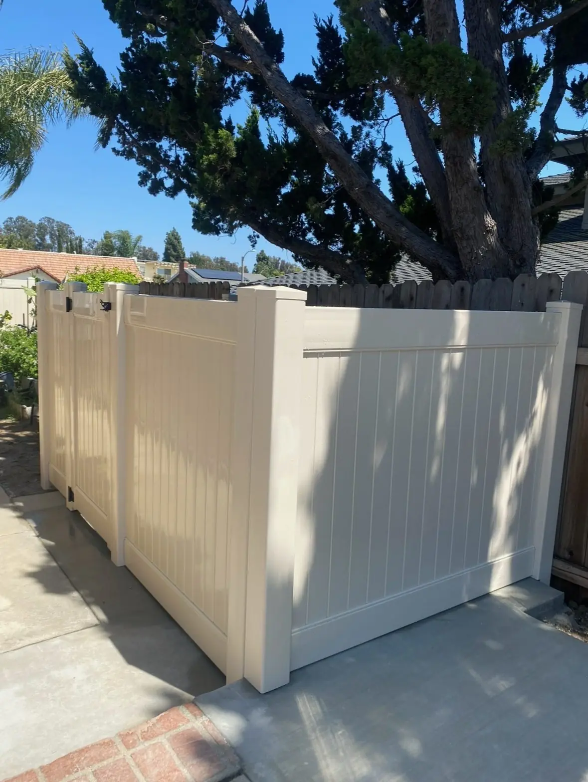 Tan vinyl trash enclosure with gate on a concrete pad