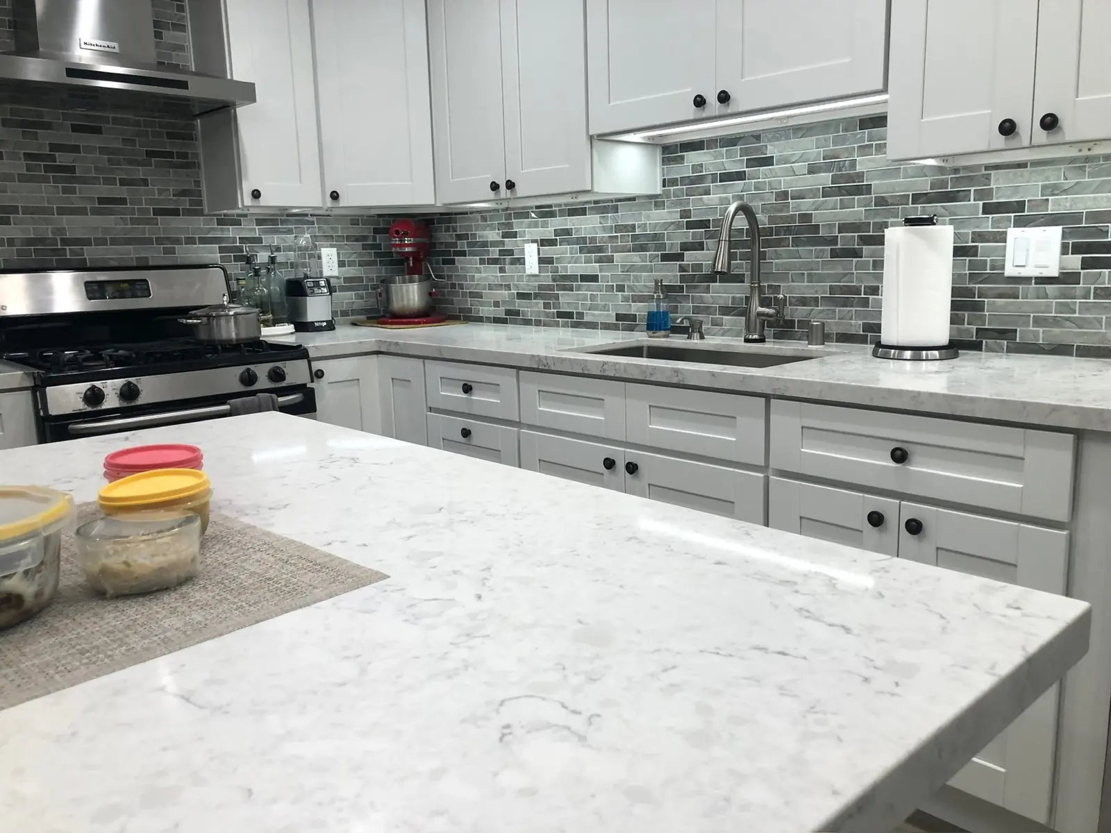 Quartz countertops, white shaker cabinets and stone mosaic backsplash
