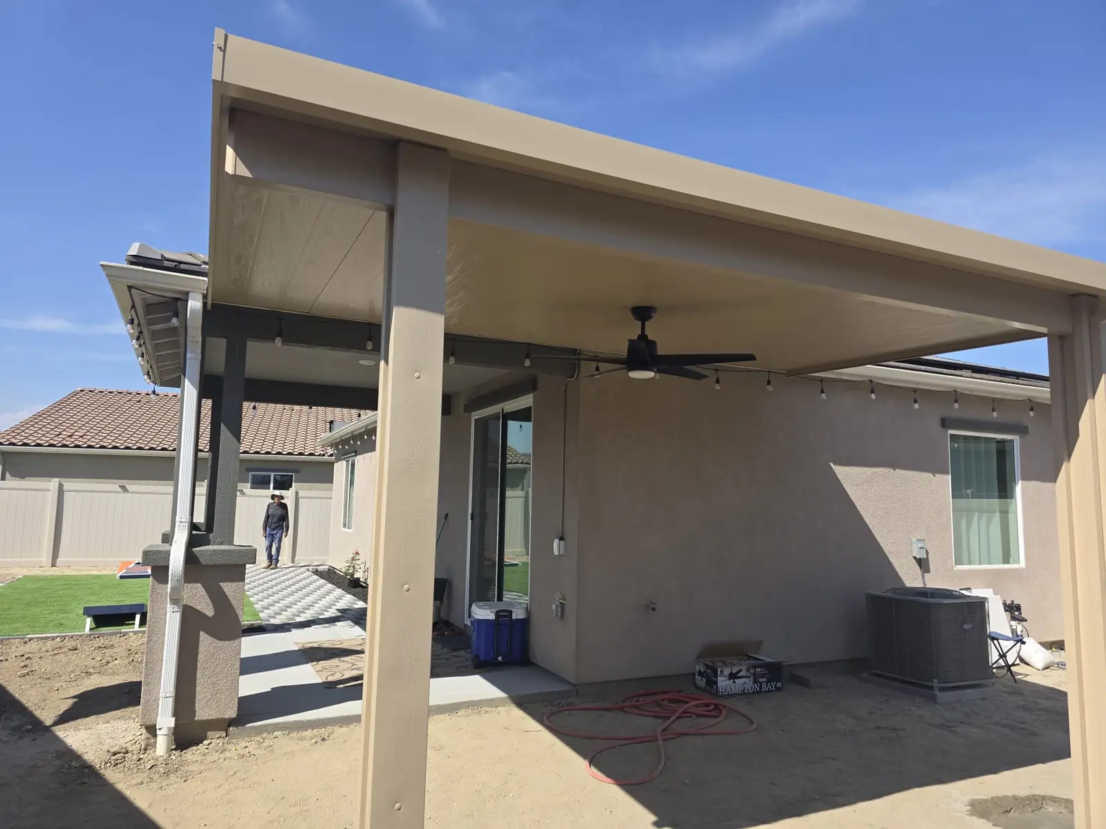 Tan solid patio cover with ceiling fan on a new home