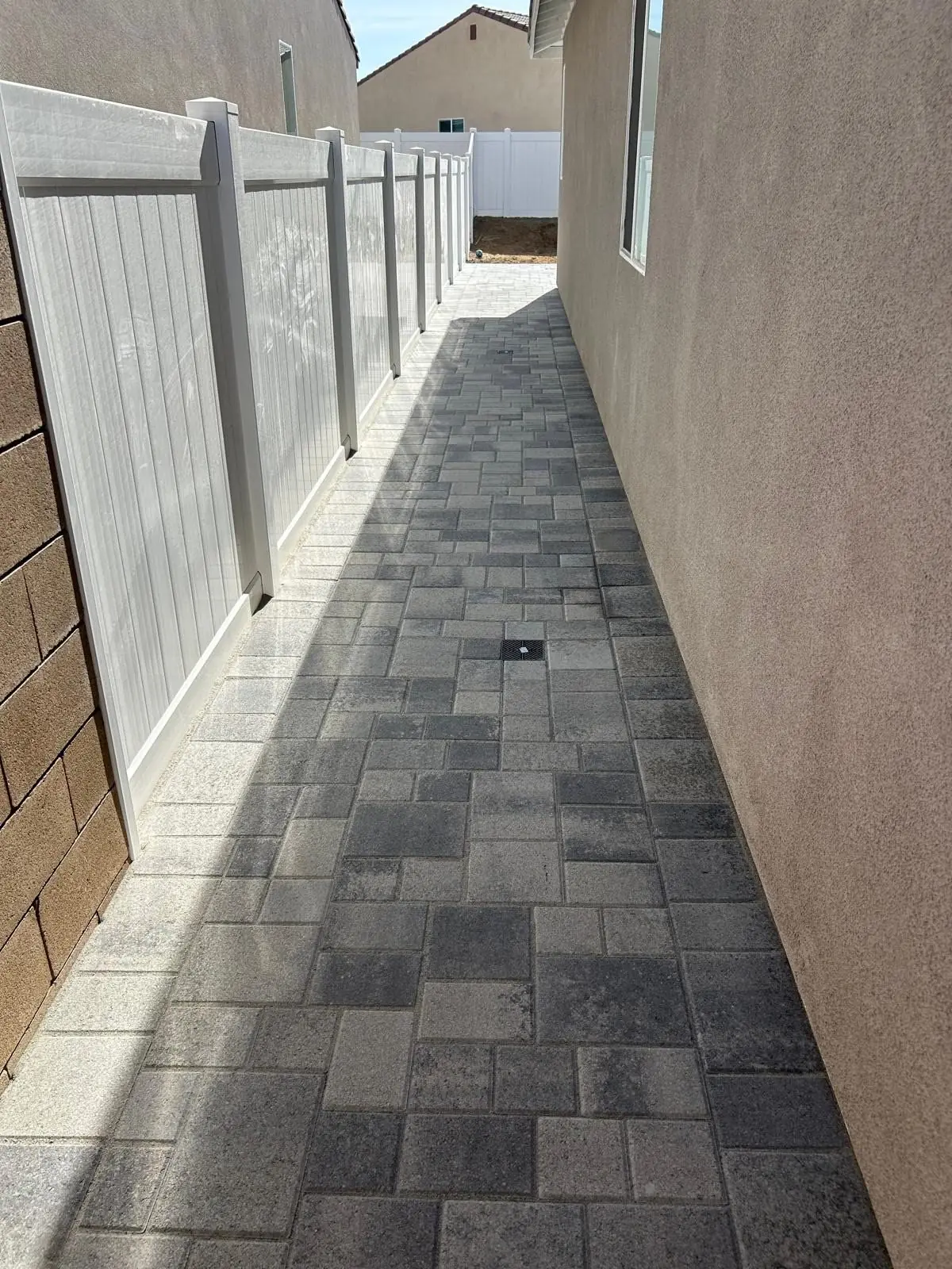 Grey paver side-yard walkway along a vinyl fence