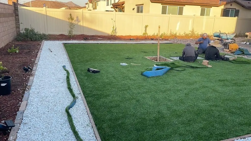 Crew finishing a backyard turf install with a white rock border