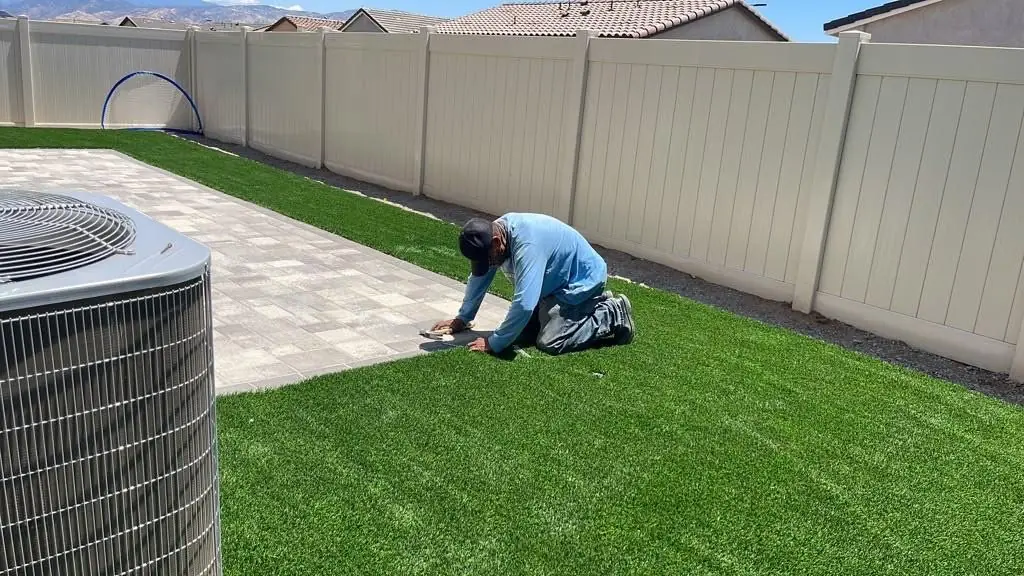 Installer finishing artificial turf along a paver edge