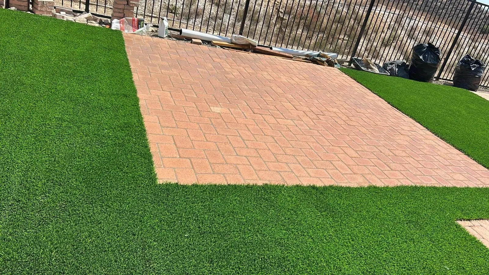 Artificial turf wrapped around a red paver patio